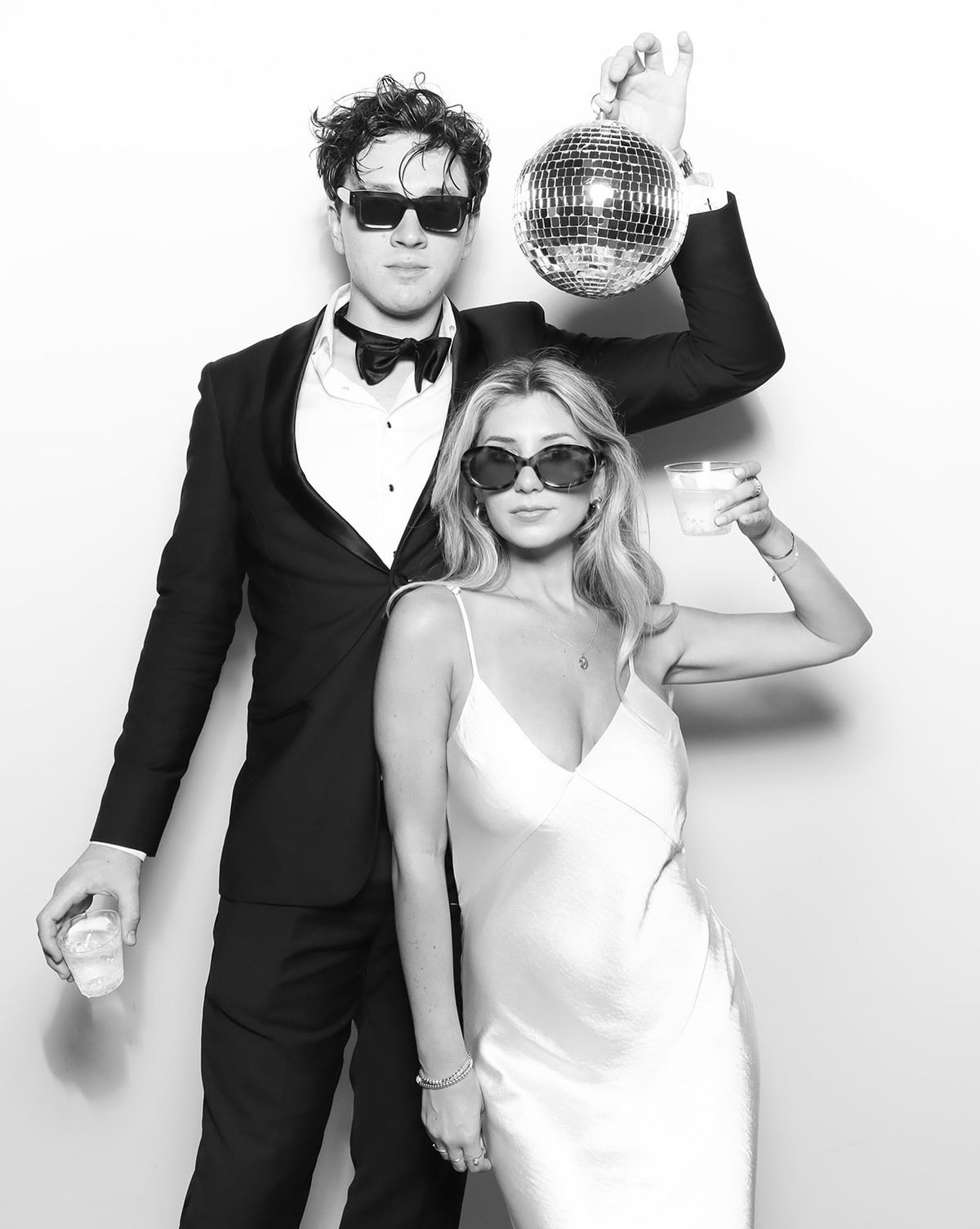 A black-and-white photo-booth print of a couple posing with a disco ball prop